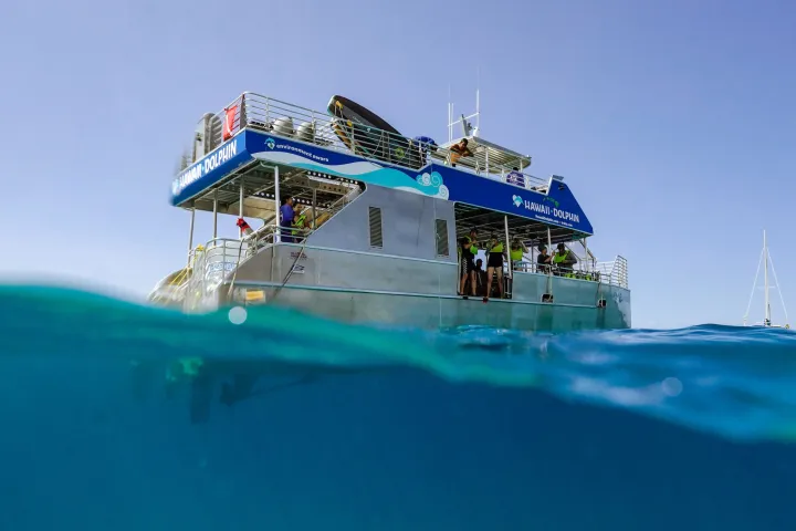 A boat named Hawaii Dolphin viewed from water level with people on board.