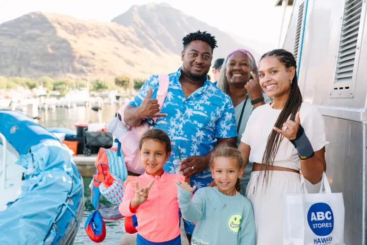 Smiling family on a dock, boats and mountains in the background.