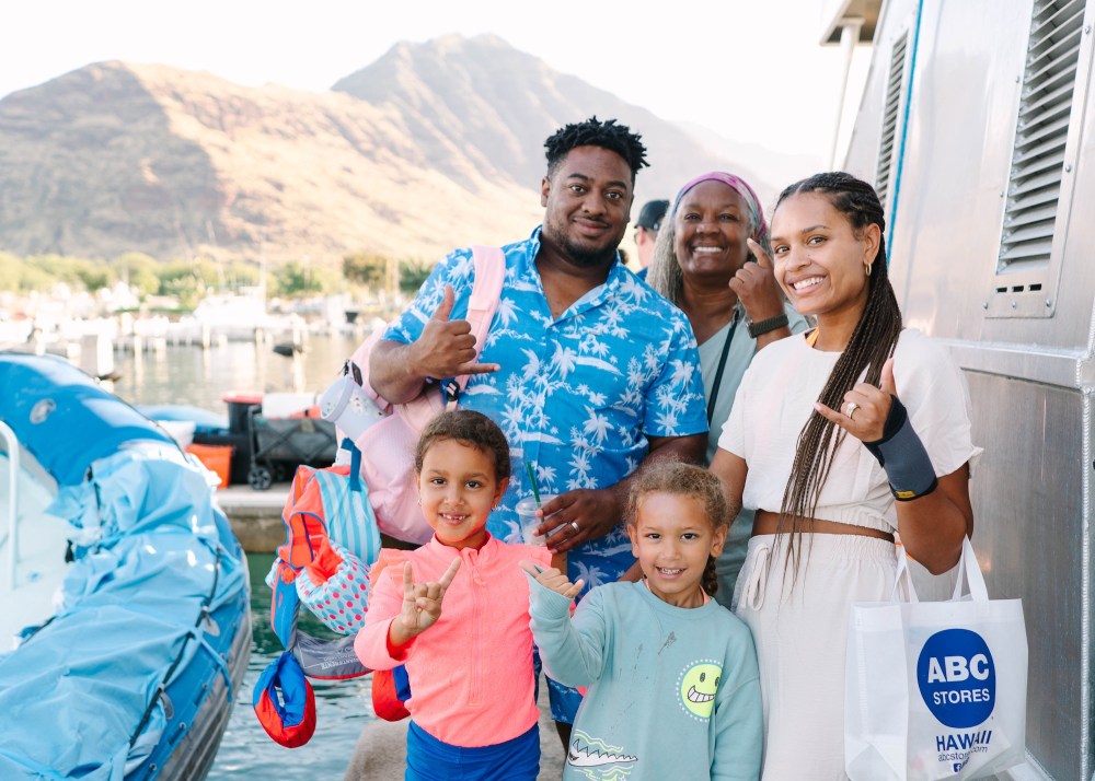 Smiling family on a dock, boats and mountains in the background.