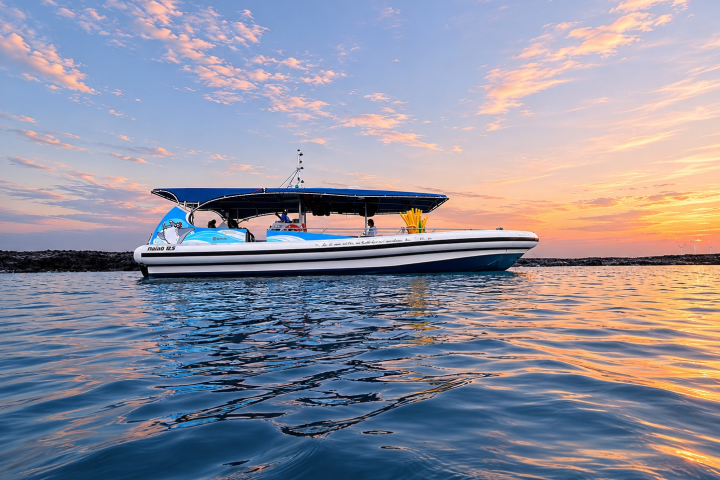 Boat on calm water at sunset with colorful sky reflections.