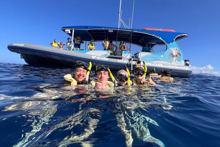 Group of snorkelers in water near a boat under a clear blue sky.