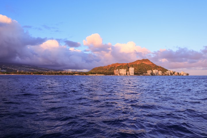Coastline with mountain and clouds at sunset, ocean in foreground.