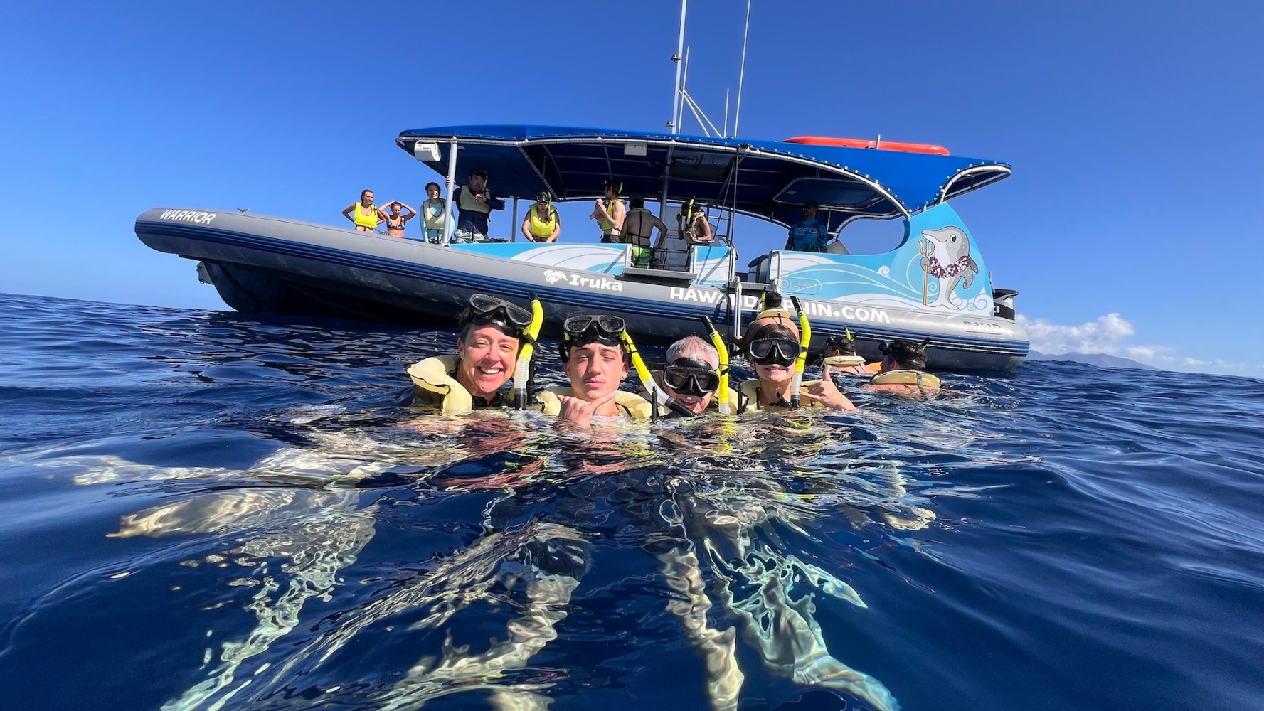 Four snorkelers in water near a boat with people onboard, under a clear blue sky.