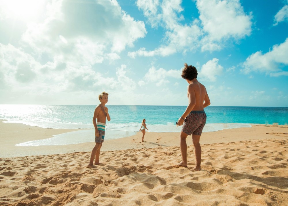 Three people on a sunny beach near the ocean, walking on the sand.
