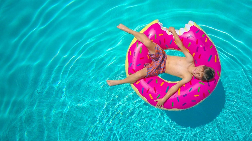 Child floating in pool on pink donut-shaped inflatable with sprinkles.
