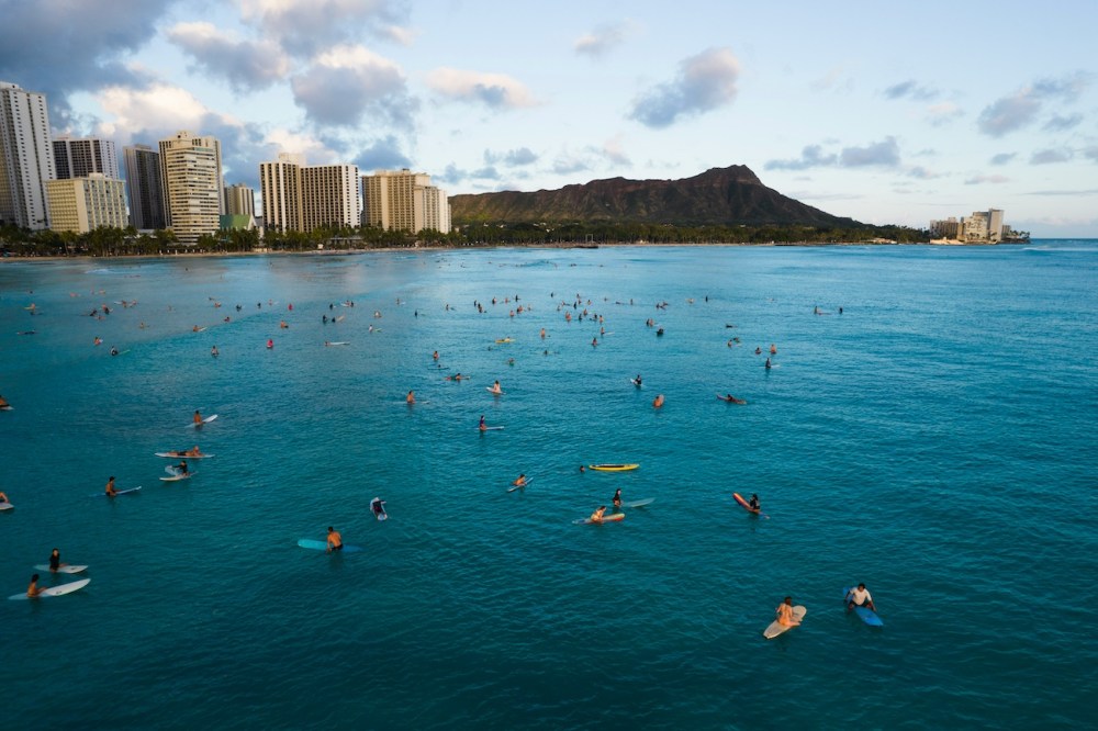 Surfers on a calm ocean with Waikiki city skyline and a mountain in the background.