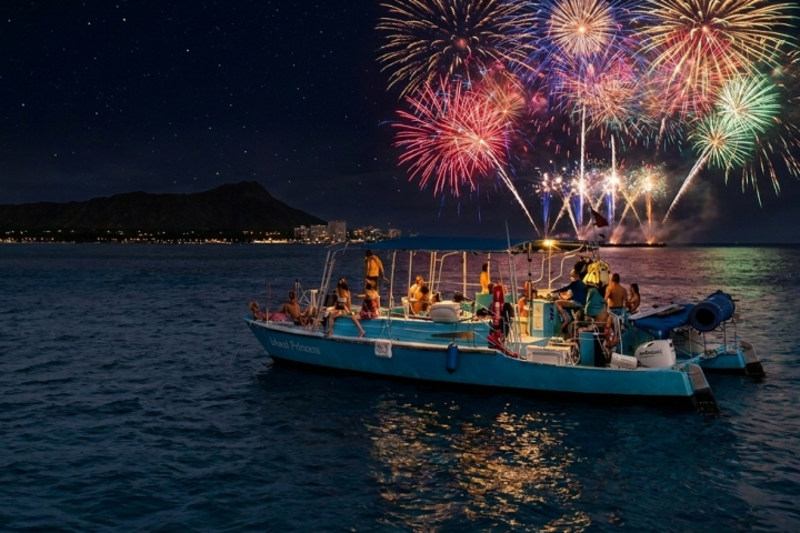 Boat with people watching fireworks over the ocean at night.