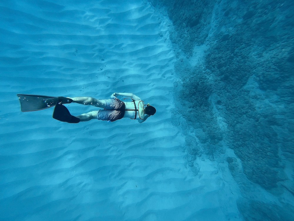 Person snorkeling underwater in clear blue ocean near a coral reef.