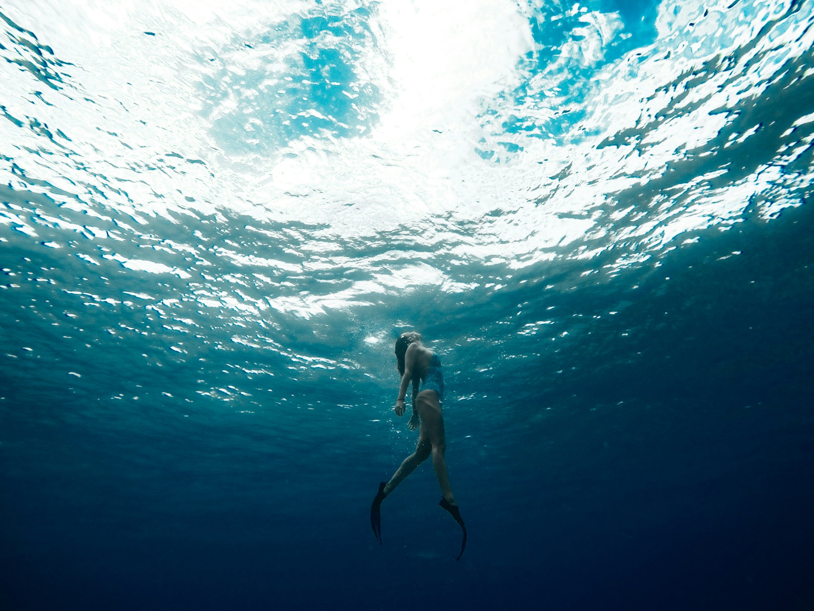 Person swimming underwater with sunlit waves above.