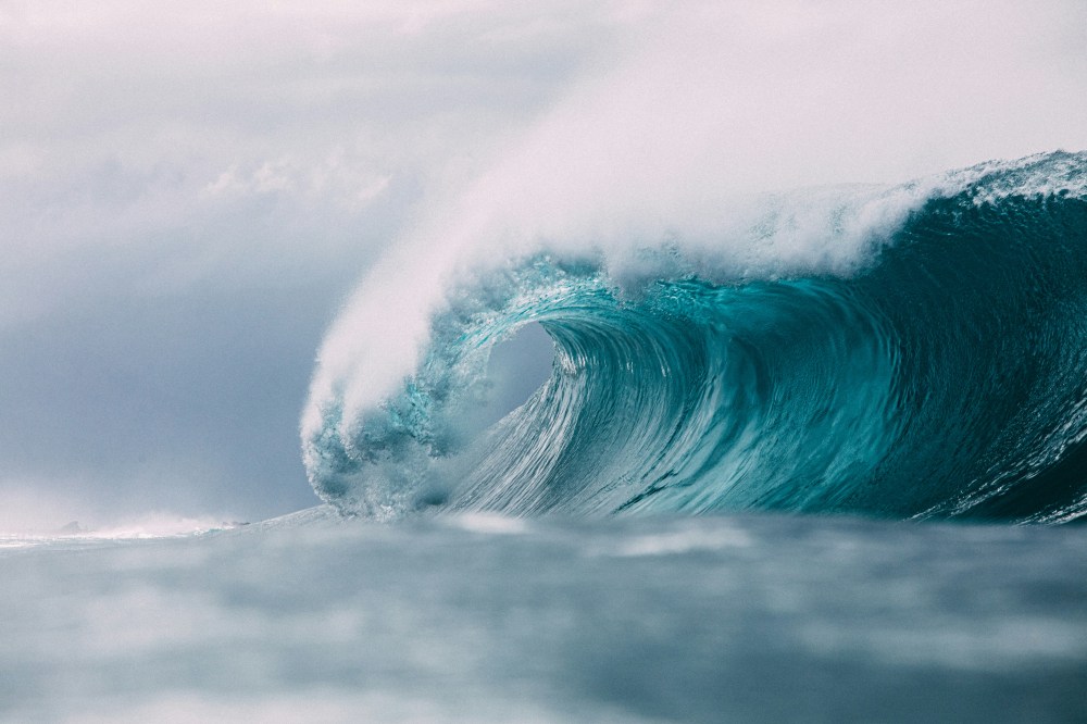 Large ocean wave curling with foam against a cloudy sky.