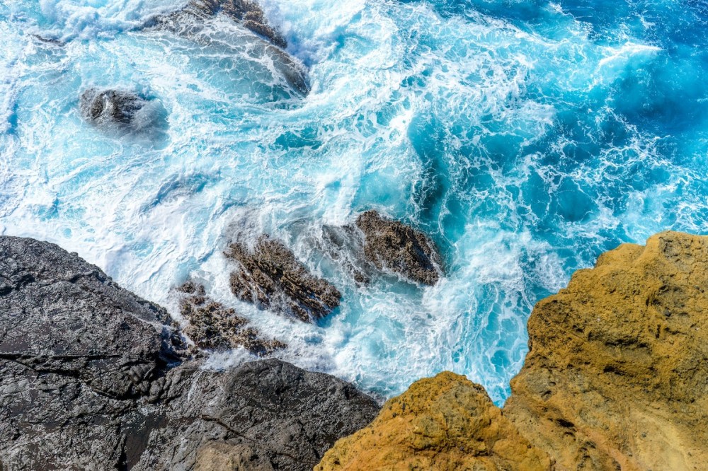 Waves crashing on rocky coastline with blue and white water.