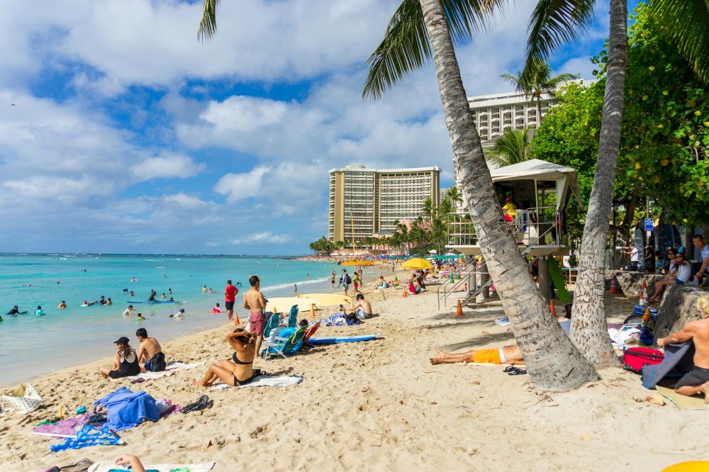 Crowded beach with people sunbathing and swimming with ocean safety on Oahu